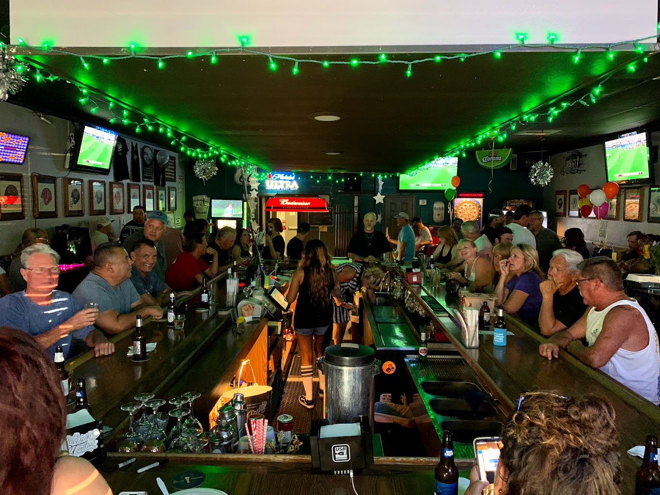 another angle of a full bar with people enjoying drinks and a game on tv
