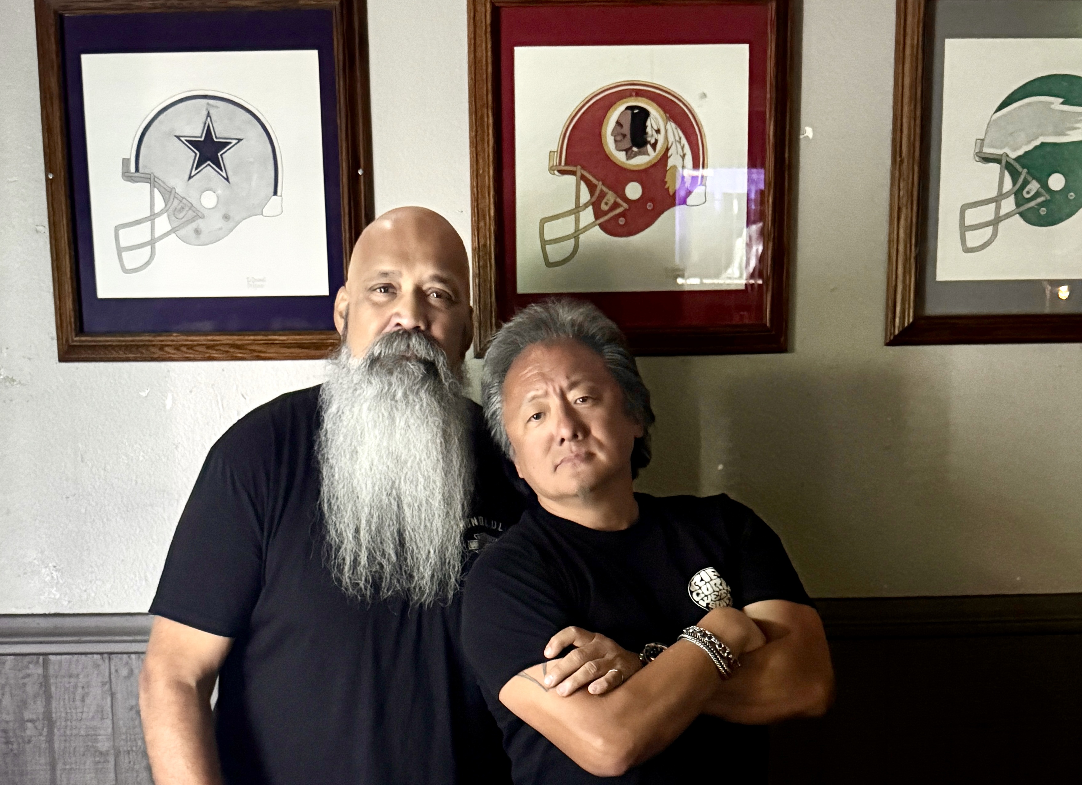 two older gents posing in front of football helmet pictures